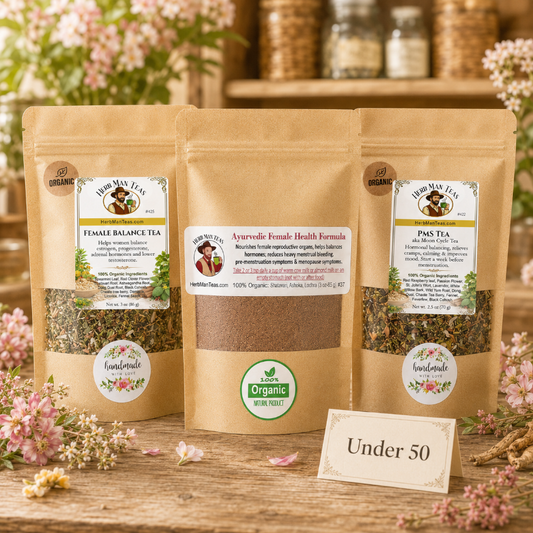 Three stand-up pouches of Herbal Vision tea products arranged on a wooden surface with pink flowers around them. The center pouch is open, showing a brown herbal powder, while the two side pouches are sealed and display labels for Female Balance Tea, Ayurvedic Female Health Formula, and PMS Tea.